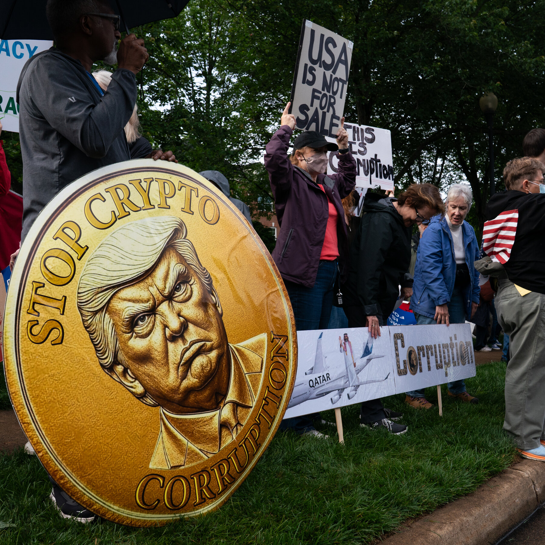 Protesters hold signs including a large "Stop Crypto Corruption" coin with Trump's face.