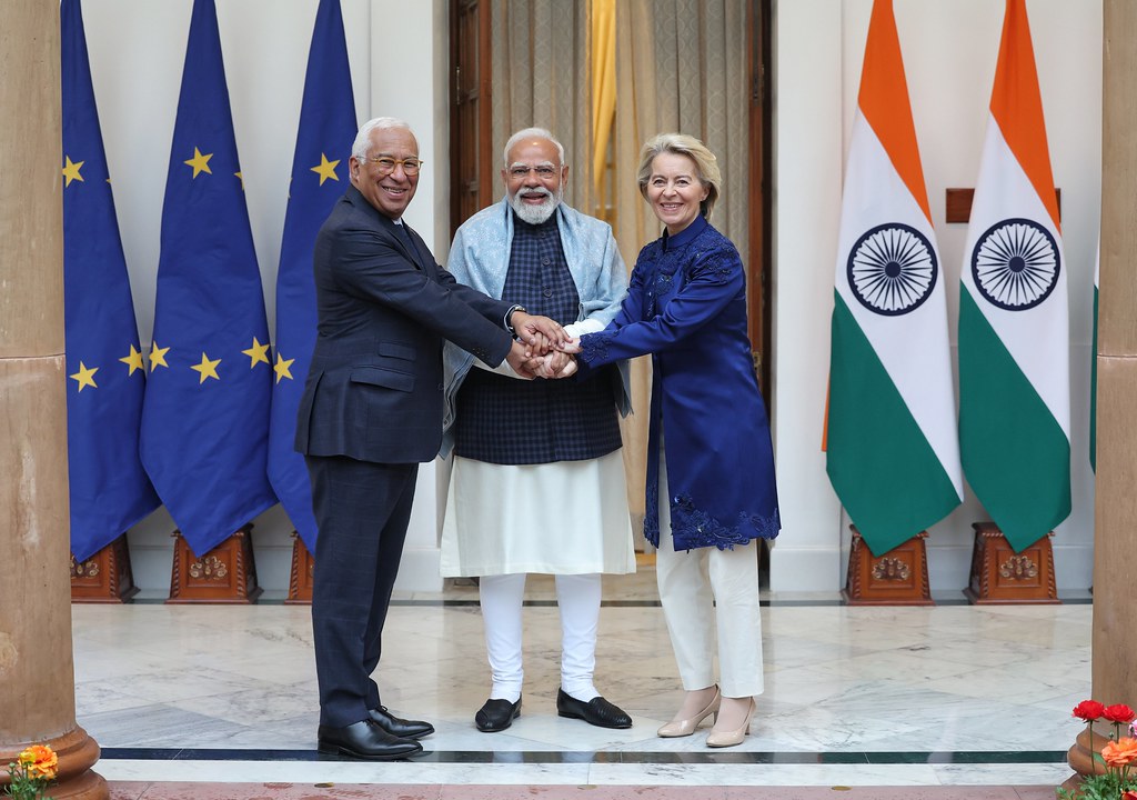 Three politicians shaking hands with Indian flags and EU flags in the background