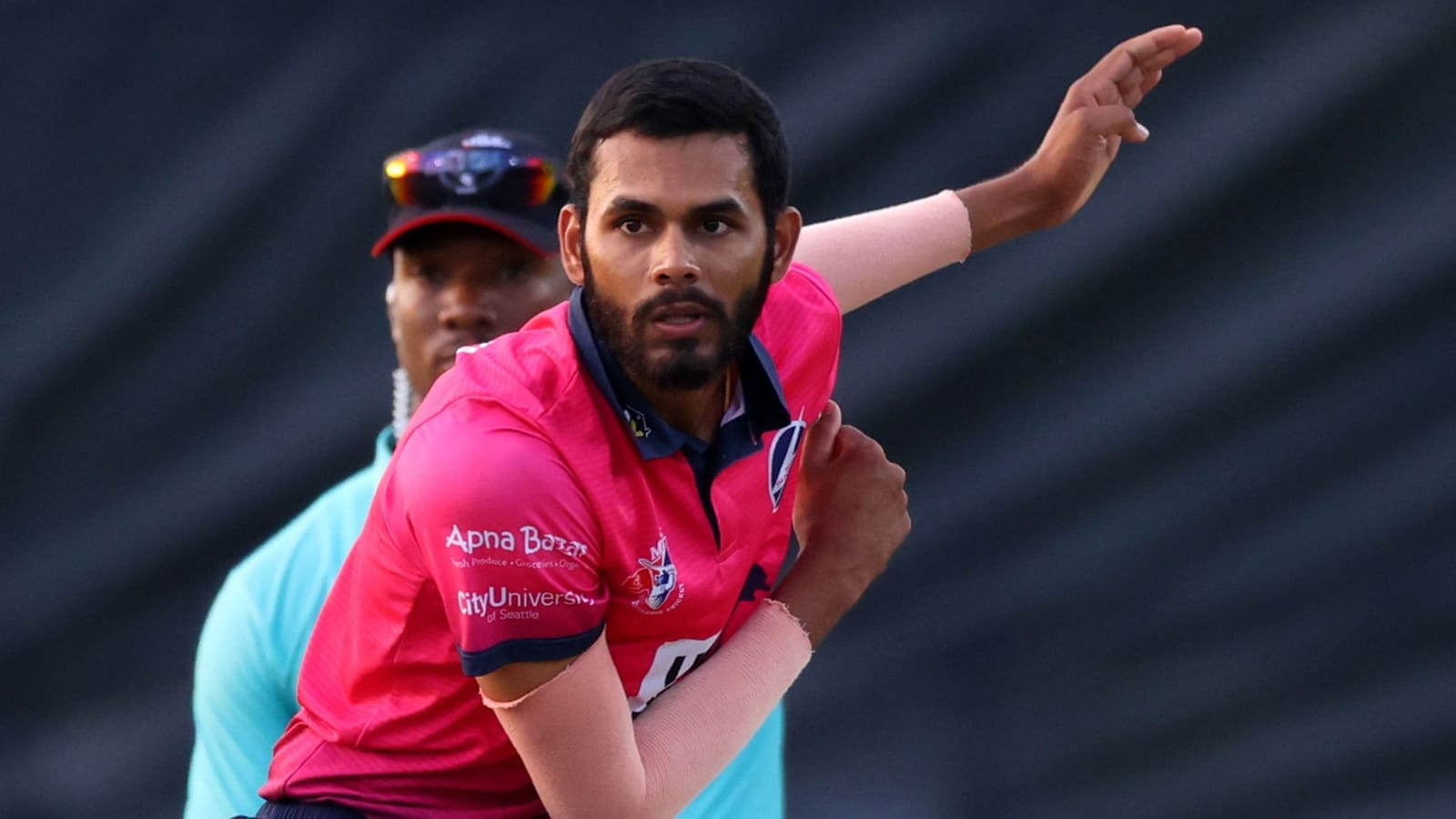 Cricketer Akhilesh Reddy in a pink jersey, bowling during a sports match.