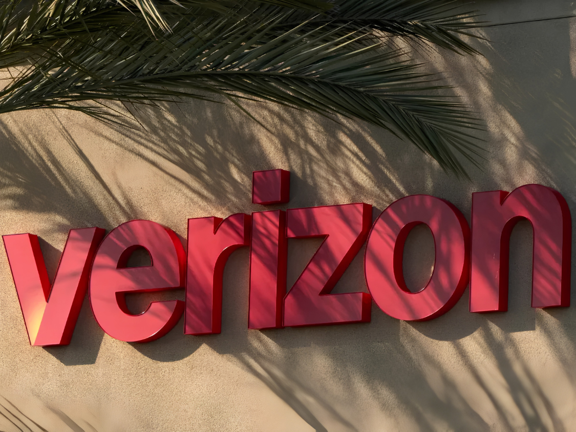 Verizon logo on a building exterior, with palm fronds casting shadows.