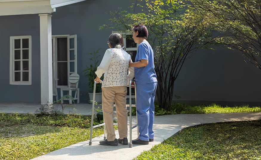 Caregiver assists elderly woman with walker outside, immigration rules impact