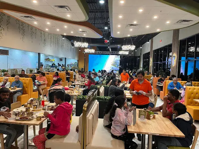 Indian restaurant with families dining, featuring a large screen showing a beach scene.