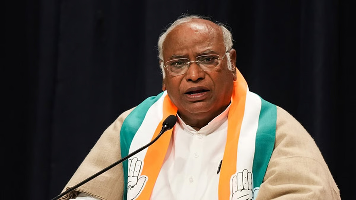 Mallikarjun Kharge speaking at a press conference, wearing a Congress sash.