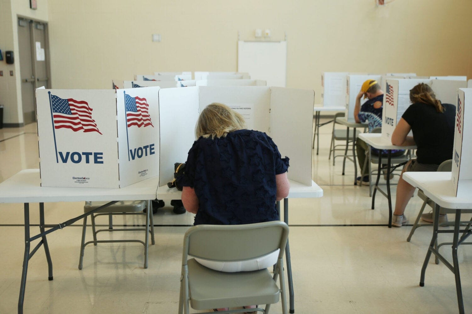 Voters in booths at a polling station, with "Vote" signs visible.