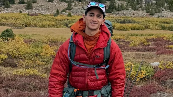 News: Man in red jacket hiking in a mountainous landscape.