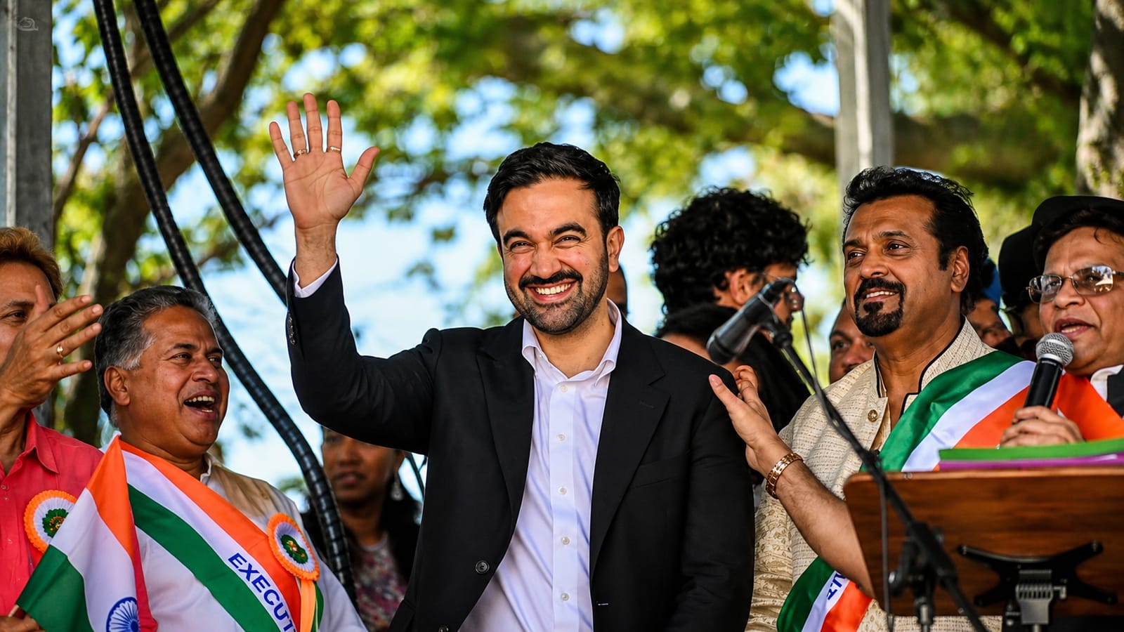 NYC Mayor Mamdani waves at the Queens India Day Parade, surrounded by supporters.