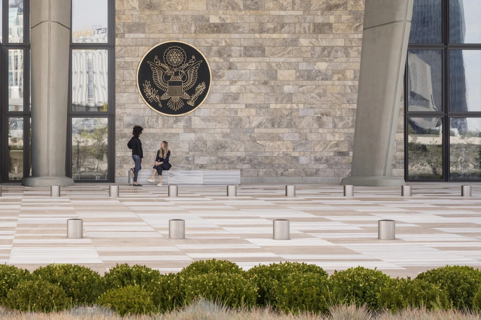 US Embassy exterior with Great Seal, two people seated