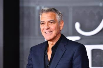 George Clooney, honored for his culture contributions, smiles in a suit.