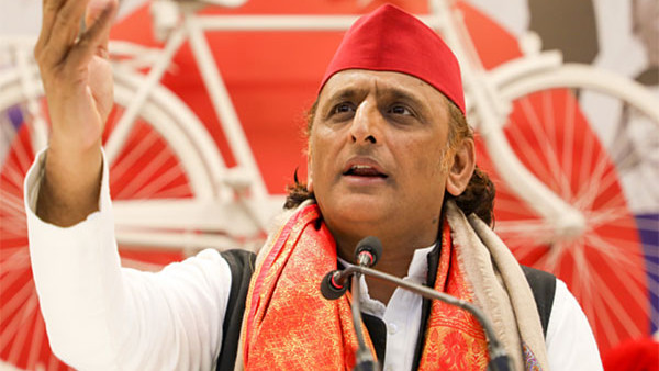 Akhilesh Yadav speaking at a podium, with a red bicycle symbol in the background.