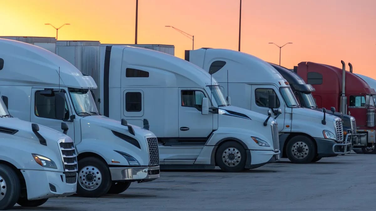 White semi-trucks parked in a lot at sunset, relevant to trucking industry fraud and visa issues.