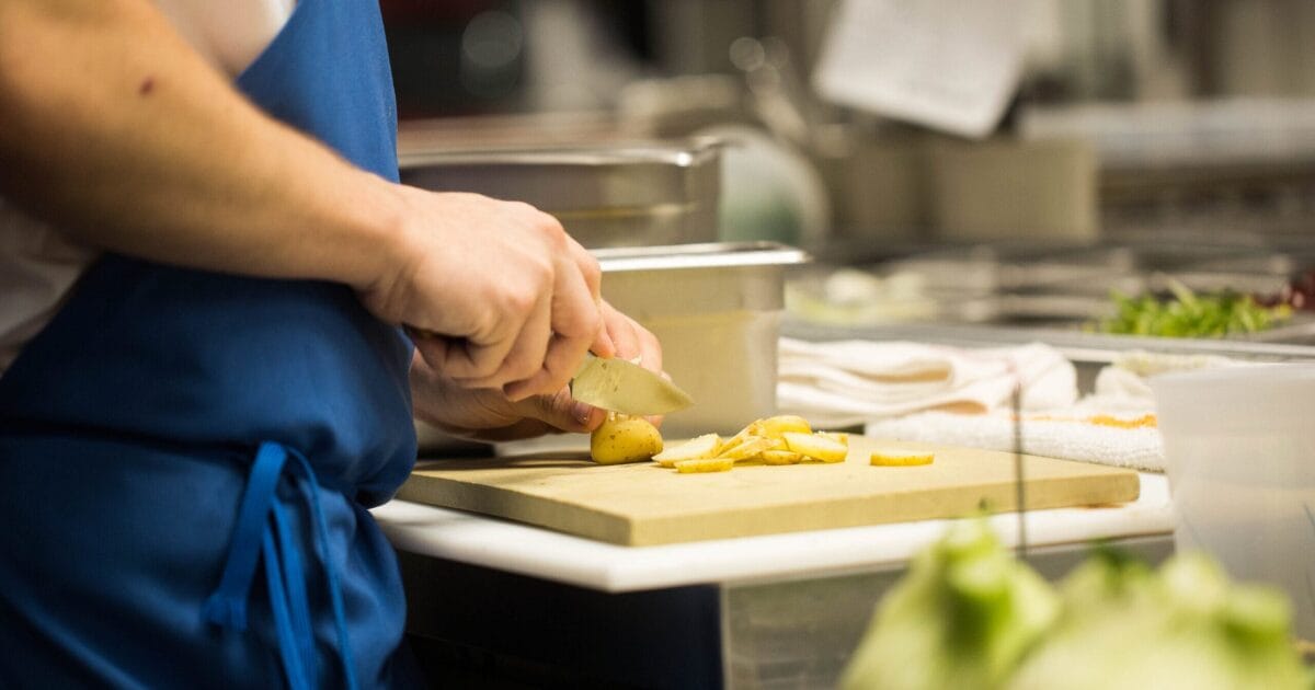 Chef in blue apron slices potatoes in Texas restaurant kitchen, facing staff shortages.