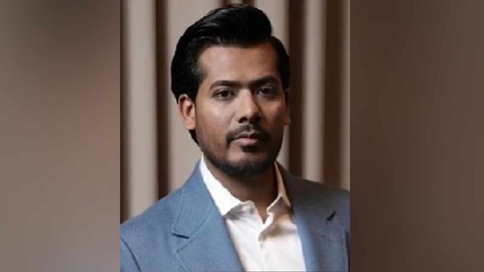 Man in blue suit, possibly involved in India's pursuit of Mahadev betting app kingpin.