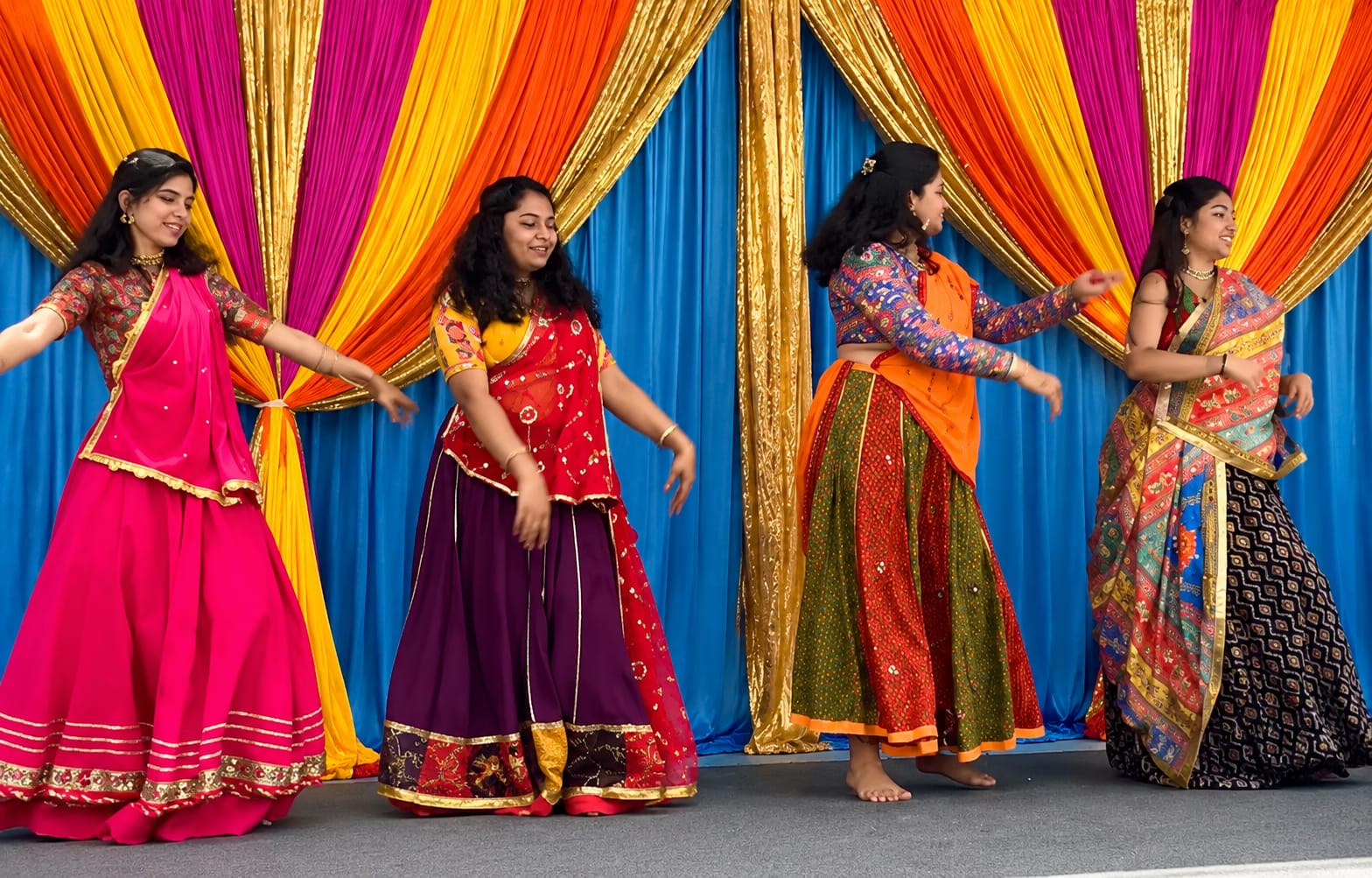 Four women in colorful Indian attire dancing at a Heritage of India festival.