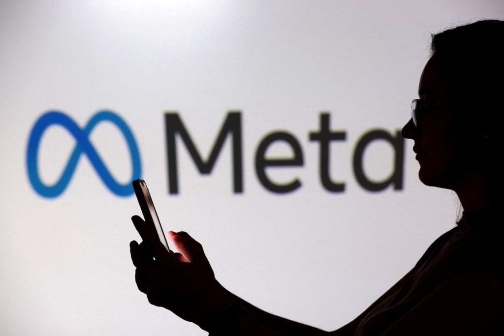 Silhouette of a person holding a smartphone in front of the Meta logo, news.