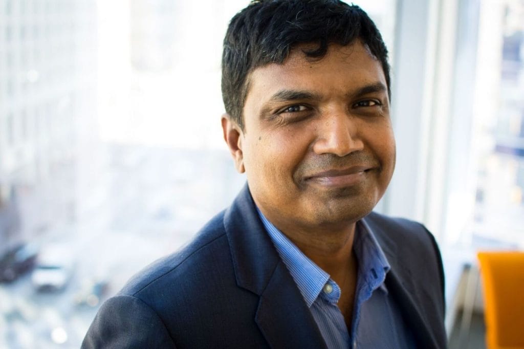 Indian American AI professor smiles, representing tech innovation.